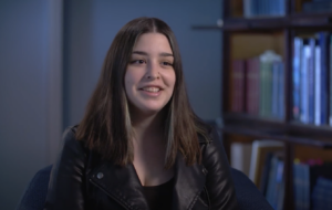 A smiling girl with long dark hair looks just off camera